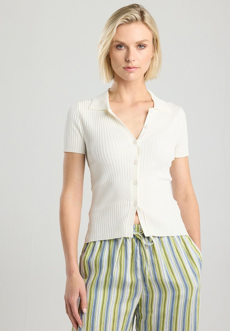 White ribbed short-sleeve cardigan with a collared neckline and buttons, paired with green and blue striped pants featuring a drawstring.