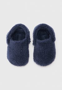 Un par de zapatillas de casa de color azul marino, suaves y tipo slip-on, con puntera redonda, sobre un fondo blanco.