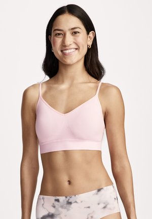 Smiling woman with long dark hair wears light pink bralette and high-waisted, marble-patterned leggings, standing against a plain background.