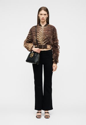 Γυναίκα με καφέ μοτίβο cropped μπουφάν, μαύρο ψηλόμεσο παντελόνι, μαύρα σανδάλια και κρατώντας μια μαύρη τσάντα χειρός με χρυσές λεπτομέρειες.