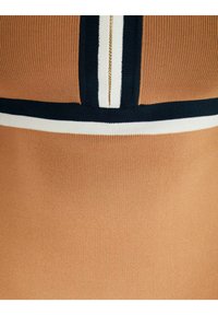 Brun räfflad tyg med marinblå och vita horisontella ränder. Slät textur, figurnära design. Har kontrasterande randdetaljer nära halsringningen.