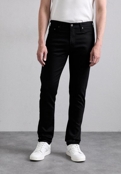 Black denim jeans with a slim fit, featuring a standard five-pocket design and metal hardware. Paired with white sneakers.