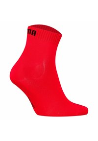 Röd ankelsocka med ribbad midja, tillverkad av ett mjukt material, med svart logotyptext nära toppen. Detaljerad formning av tå och hälen.
