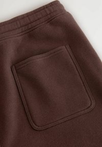 Pantalon de survêtement marron avec une poche plate à l'arrière, fabriqué en tissu doux. Présente un design simple sans embellissements ni motifs.