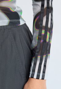 Sporty long-sleeve shirt with a mesh pattern in gray, featuring colorful accents and three black vertical stripes on the arm. Black pants with a smooth finish.