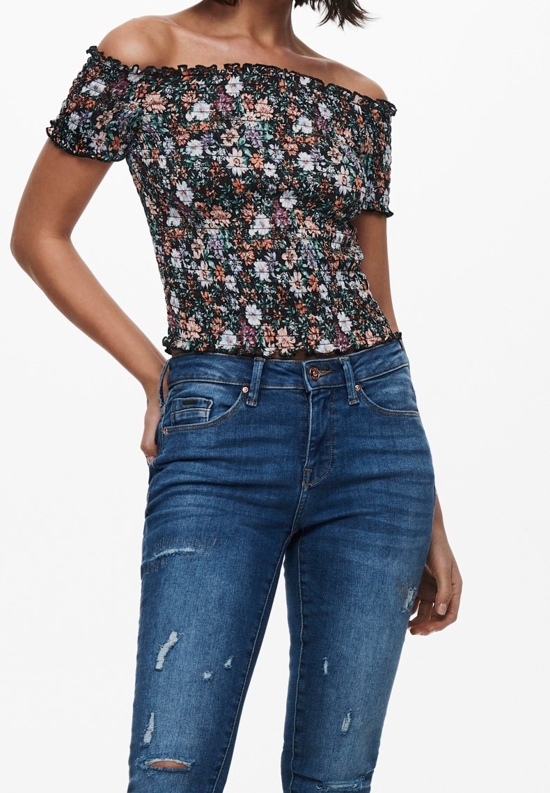 Olkalta paljastava kukkakuosiset paita, jossa on musta smokkikangas, jossa on valkoisia ja oransseja kukkia, yhdistettynä kulutettuihin sinisiin farkkuihin.