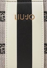 Liu Jo bag featuring a beige and black striped design, textured canvas, and gold logo detail. Edges are stitched in white thread.