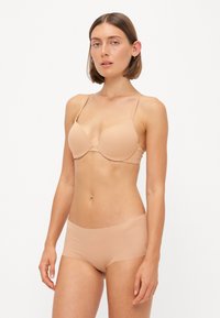 Nude padded bra with thin adjustable straps and seamless design, paired with matching high-waisted briefs in a smooth, stretchy fabric.
