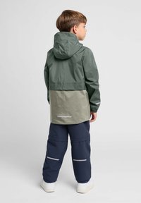 Wasserabweisende Jacke mit Kapuze, bestehend aus einem grünen oberen Teil und einem hellgrauen unteren Teil, reflektierenden Akzenten und elastischen Bündchen.