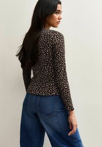 Top a maniche lunghe con stampa animale nei toni del marrone e del nero, dal design aderente, abbinato a pantaloni in denim blu a vita alta, vista posteriore.