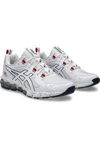 Zapatillas deportivas blancas con una parte superior de material mixto, con acentos en color azul marino y detalles en cordones rojos, suela salpicada y diseño de amortiguación de gel.