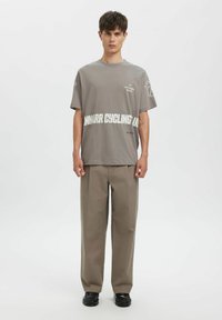 Grå bomulls-T-skjorte med hvit tekst, korte ermer og rund hals, kombinert med beige vidbukser og svarte sko.