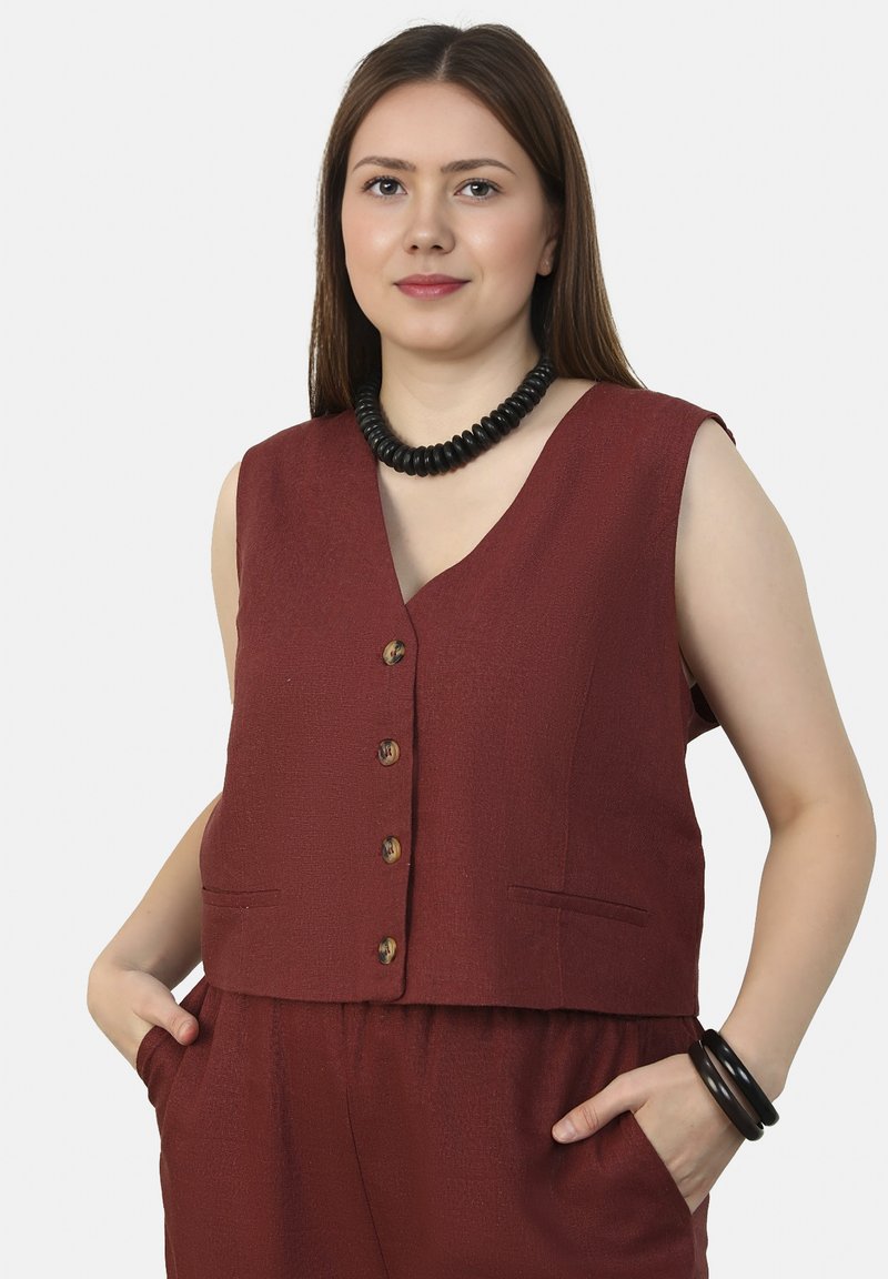 Bordeaux mouwloze vest met een diepe V-hals, knopen aan de voorkant en zijzakken. Gladde textuurstof en houten knoopaccenten.