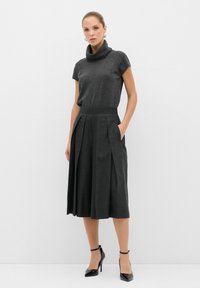 Grå kofttröja med cowl-nacke i kombination med en högmidjad, veckad grå kjol. Outfiten har sidofickor och kompletteras med svarta högklackade skor.