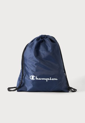 Marineblauwe Champion-trekkoordtas met zwarte koorden, bovenaan samengetrokken, wit Champion-logo op de voorkant, effen lichte achtergrond.