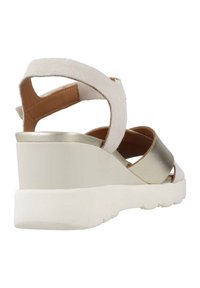 Sandalias de cuña en blanco y dorado metálico, con suaves correas de ante y una suela de goma blanca sólida. Diseño abierto por detrás.