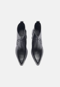 Bottines en cuir noir avec un bout pointu, fermeture éclair sur le côté et broderies décoratives sur le dessus. Texture lisse avec un design épuré.