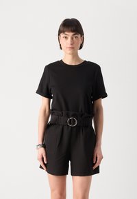T-shirt noir à manches courtes avec des manches retroussées, associé à un short taille haute avec une large ceinture et une boucle circulaire, le tout en noir uni.