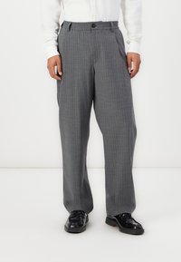 Gray, plaid trousers with a relaxed fit, featuring an elastic waistband and a button closure, paired with black shoes.