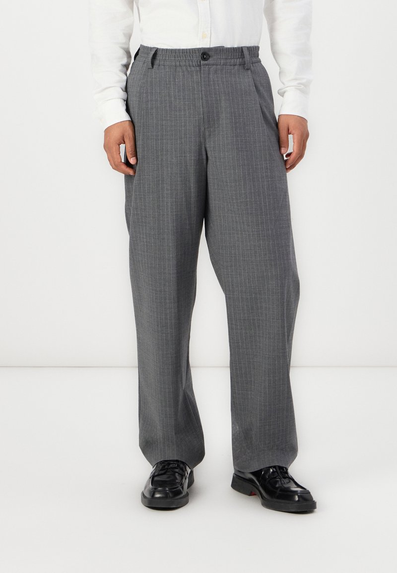 Gray, plaid trousers with a relaxed fit, featuring an elastic waistband and a button closure, paired with black shoes.