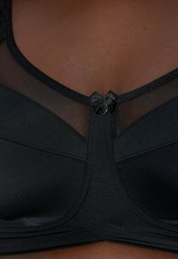 Reggiseno nero con pannello in rete sulla parte superiore, tessuto liscio e piccolo fiocco decorativo al centro con chiusura a bottone.