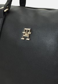 Schwarze Lederhandtasche mit strukturiertem Finish und einem goldfarbenen Logo-Detail. Das Design umfasst einen Reißverschluss und robuste Tragegurte.