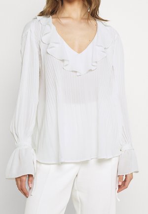 Camicia bianca con colletto arricciato e texture plissettata; maniche lunghe con polsini svasati. Tessuto morbido e leggero. Design semplice ed elegante.