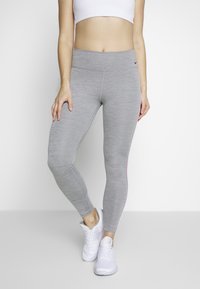 Szare legginsy sportowe o gładkiej strukturze, z wysokim stanem i różowym paskiem po boku, połączone z białymi trampkami.