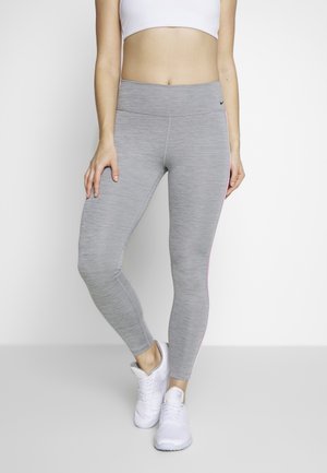 Leggings de sport gris avec une texture lisse, une taille haute et une rayure rose sur le côté, associés à des baskets blanches.
