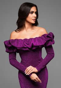 Violetti olkapäältä paljastava mekko, jossa on röyhelökaulus, pitkät tiukasti istuvat hihat ja teksturoitu kimaltava viimeistely. Malli poseeraa kädet ristissä.