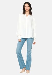 Blusa bianca con bottoni frontali, maniche lunghe e pieghe sottili. Abbinata a jeans a zampa d'elefante blu chiaro e scarpe beige.