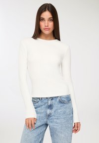 Biała bluzka z długim rękawem wykonana z gładkiego materiału, z okrągłym dekoltem i dopasowanym krojem, w połączeniu z jasnoniebieskimi dżinsami z wysokim stanem.