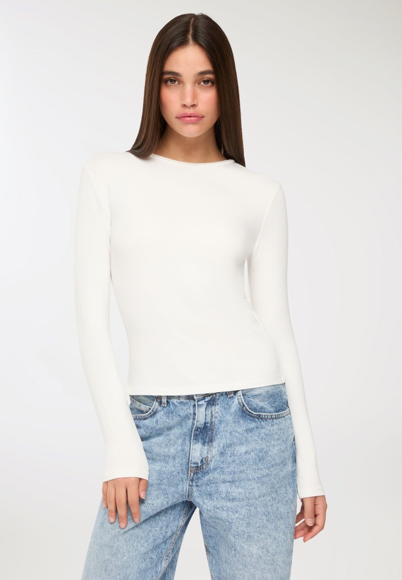 Biała bluzka z długim rękawem wykonana z gładkiego materiału, z okrągłym dekoltem i dopasowanym krojem, w połączeniu z jasnoniebieskimi dżinsami z wysokim stanem.