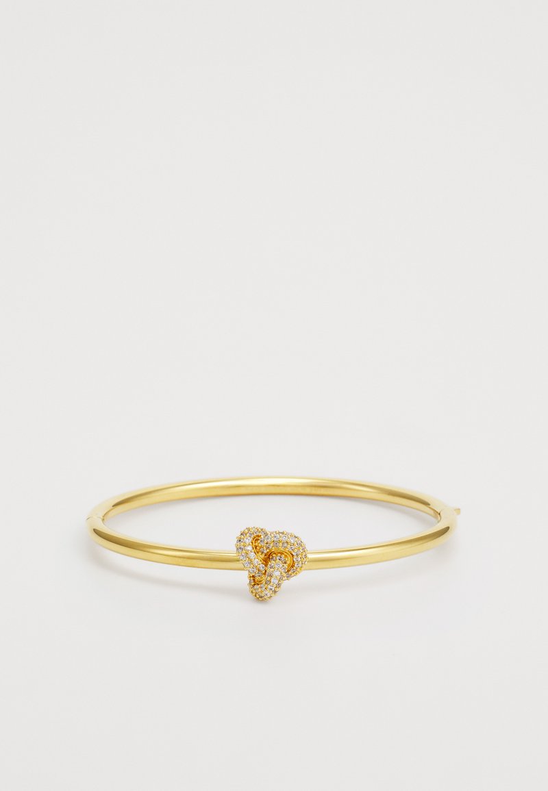Pulseira de ouro com uma banda lisa e arredondada. Apresenta um design de nó entrelaçado cravejado com cristais transparentes. Simples e elegante.