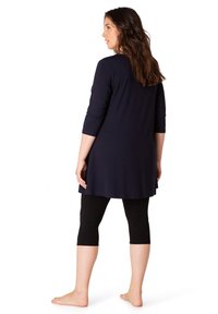 Marine tuniek met driekwartmouwen, ontspannen silhouet, gecombineerd met zwarte capri leggings. Glad materiaal, knie-lange zoom, minimale details.