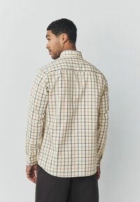 Camisa de manga larga en crema con un patrón de cuadros marrones, verdes y naranjas, que presenta un cuello estándar y puños con botones.