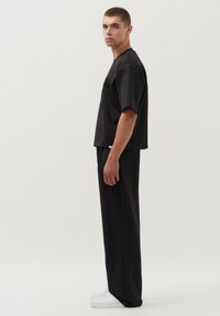 Zwart shirt met korte mouwen en losse broek van een matte stof, met een relaxte pasvorm en minimalistisch ontwerp, gecombineerd met witte sneakers.
