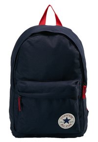 Námořnická modrá batoh Converse All Star s červenými zipy a horním madlem, přední kapsa na zip a kulatou bílou logo nášivkou.