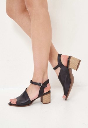 Sandales à talons ouvertes en cuir noir avec un talon bloc. Dotées d'une bride de cheville avec une boucle et d'un design lisse et élégant.