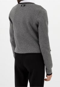 Harmaa neulepaita, jossa on lyhyt malli, ribbireunus ja musta sydämenmuotoinen yksityiskohta takana kaula-aukossa. Suuri tekstuuri.