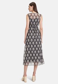 Maxikleid in Schwarz mit einem weißen Blattmuster. Ärmelloses Design, taillierter Schnitt mit Kordel, transparenter Überzug, glatte Textur. Blockabsatzschuhe.