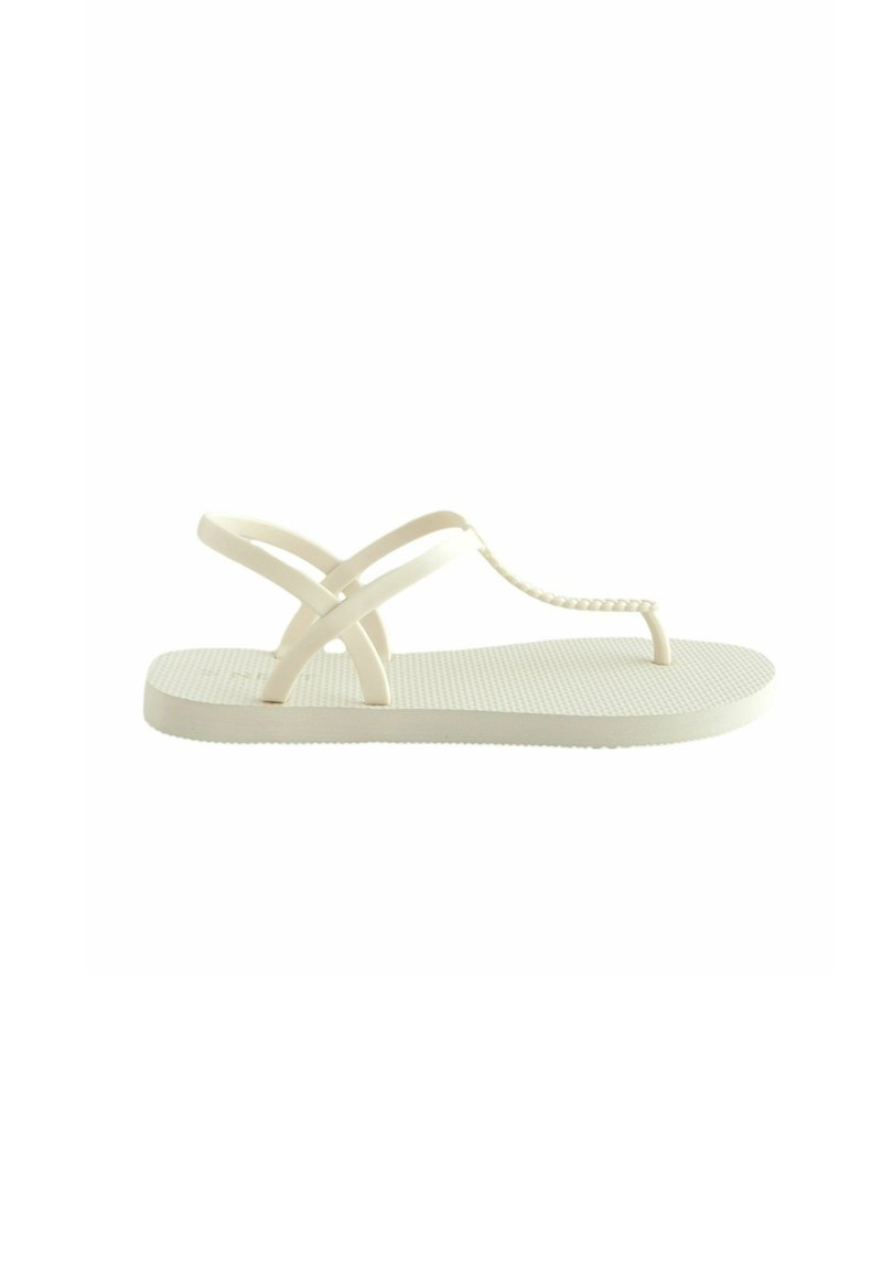Hellbeige Flip-Flops mit einer strukturierten Gummisohle, einem schlanken T-Riemen und überkreuzten Riemen für zusätzlichen Halt. Einfaches und minimalistisches Design.