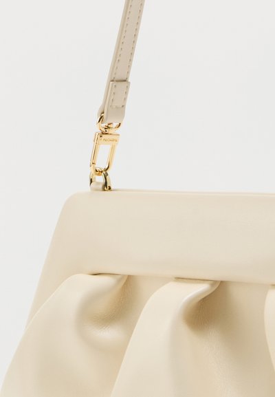 Λουρί μπεζ δερμάτινης τσάντας, στερεωμένο με χρυσό μεταλλικό κούμπωμα σε τσάντα με μαλακές ρελιασμένες δερμάτινες λεπτομέρειες.