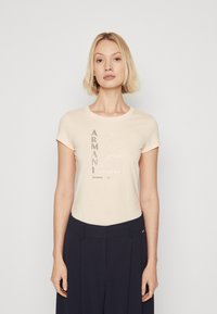 Ανοιχτό μπεζ κοντομάνικο μπλουζάκι με στρογγυλή λαιμόκοψη. Διαθέτει γραφικό σχέδιο μικτής υφής σε διάφορες αποχρώσεις και στυλ, κεντρικά τοποθετημένο στο μπροστινό μέρος.