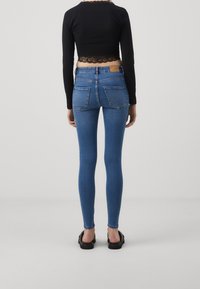 Jeans ajustados de color azul con un lavado medio, bolsillos traseros y un parche de cuero en la cintura. Combinados con un top negro cropped y sandalias planas.