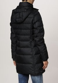 Abrigo puffer negro con capucha, con costuras acolchadas, bolsillos laterales y diseño de longitud media. Textura suave y brillante.