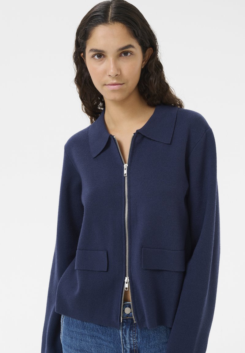 Marinblå zip-up cardigan i mjukt material, med klassisk krage, två framfickor och avslappnad passform.