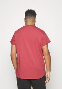 T-shirt à manches courtes, col rond, de couleur rouge atténuée, avec une coupe décontractée et un ourlet droit. Tissu en coton doux, avec une texture lisse.