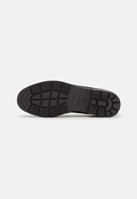 Semelle d'une chaussure noire avec des motifs de crampons profonds, la taille 37 et le logo de la marque visibles au centre.