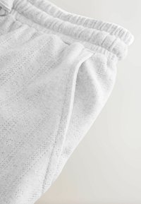 Lichtgrijze sweatpants met een gestructureerd patroon, elastische tailleband en zijzakken. De stof lijkt zacht met een ademend ontwerp.